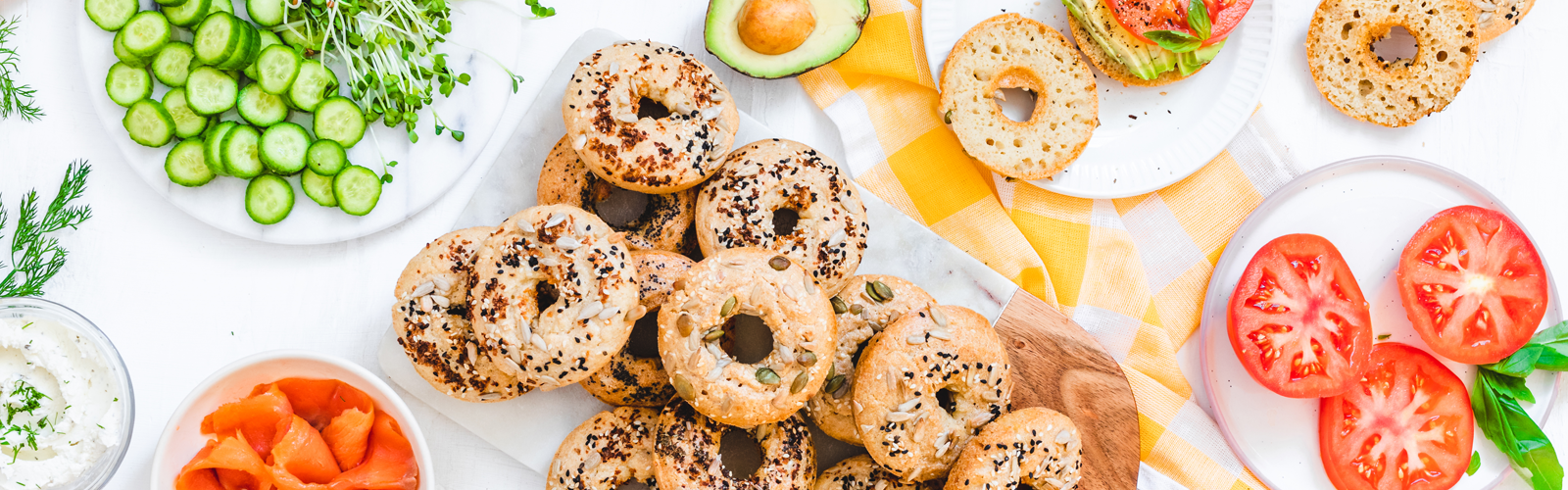 Assorted bagels sorrounded by toppings including fresh cut vegetables salmon and cream cheese