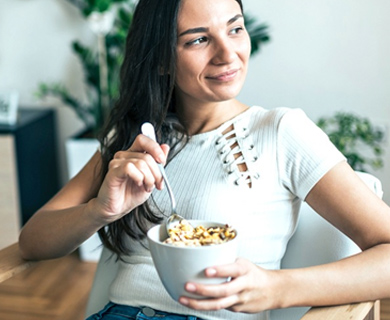 Woman sitting down holding a bowl and spoon smiling 