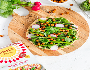 SpringVegPizza.png Spring vegetable pizza on round wooden plate on countertop with Simple Mills pizza dough box