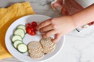 White plate with cucumber slices, cherry tomatoes and sprouted seed crackers