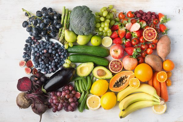 Variety of vegetables and fruits in a rainbow of colors aranged artistically on a neutral background