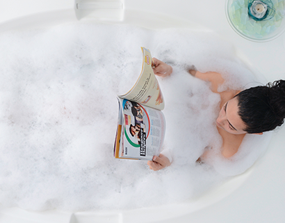 Mother enjoying bubble bath in bath tub reading a magazine