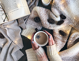 Various sweater and cozy materials, person cradling cup of hot beverage
