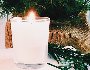 Lit white candle in a jar, christmas tree in background