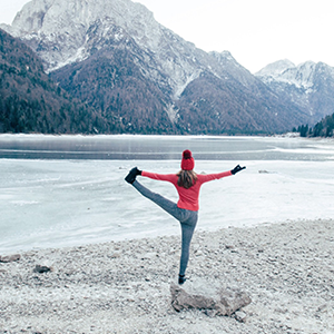 Person in balancing yoga pose in front of mountains and frozen lake
