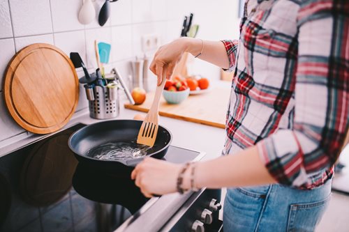 Person making a recipe in a kitchen using a pan and wooden spatula