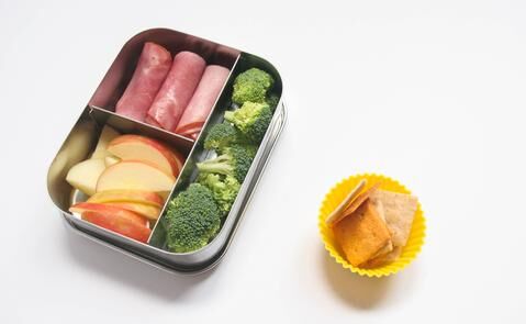 Mini lunch tin with sliced ham, apple slices and broccoli with small cup of Simple Mills almond flour crackers