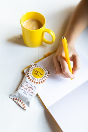 Person writing in journal using yellow pen about to eat Soft Baked Chunky Peanut butter Almond flour bars