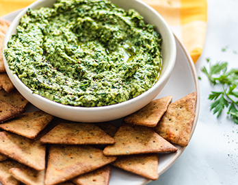 Bowl of fresh pesto dip and Simple Mills pita crackers