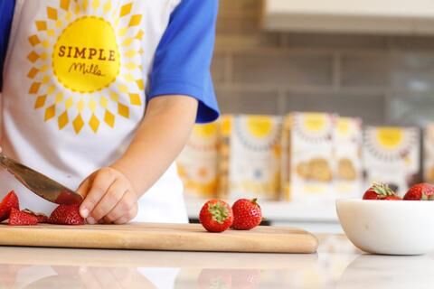 Michelle's son wearing a Simple Mills apron cutting strawberries with butter knife