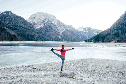 Person in balancing yoga pose in front of mountains and frozen lake 